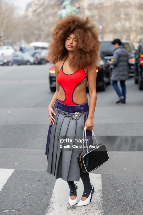PARIS, FRANCE - MARCH 11: Paola Locatelli wears red cut out shirt, grey pleated skirt, bag outside Miu Miu during the Womenswear Fall/Winter 2025/2026 as part of Paris Fashion Week on March 11, 2025 in Paris, France. (Photo by Christian Vierig/Getty Images)